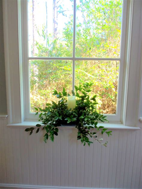 A Window Sill With A Lit Candle In The Center And Greenery On It