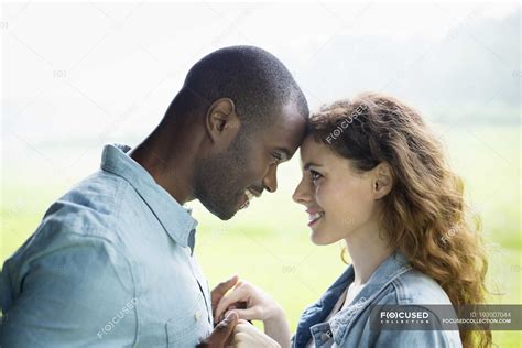 Young Couple Standing Face To Face And Holding Hands In Green Field And