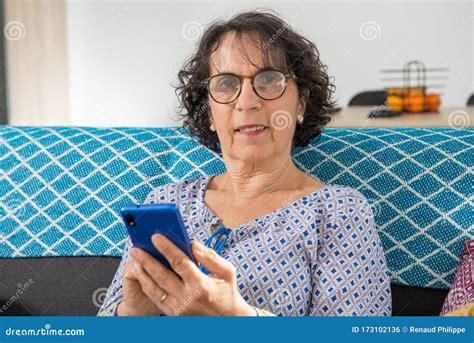 Cheerful Brunette Senior Woman Using Smartphone While Sitting On Sofa