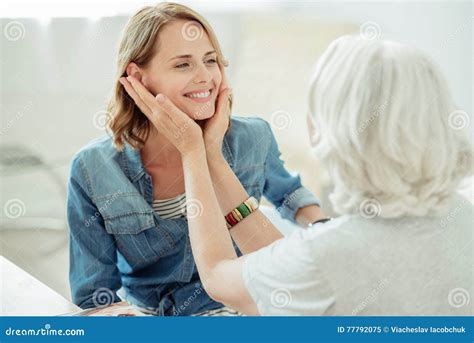 Pleasant Aged Woman Holding Cheeks Of Her Adult Daughter Stock Image
