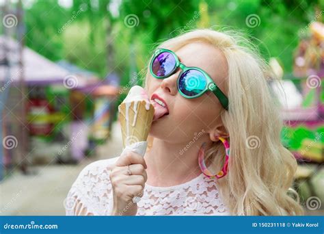 Beautiful Young Blonde Girl With Ice Cream In Her Hands Licks The Ice Cream On The Background