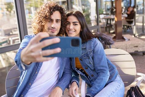 Arab Couple Taking Selfie Pictures With Their Smartphone Sitting On The Terrace Of A Bar Stock