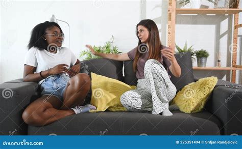 Two Young Female Roommates From College Are Sitting At Home On The Sofa