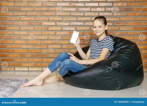 Smiling Caucasian Teen Girl Sitting In Black Bean Bag Chair Against