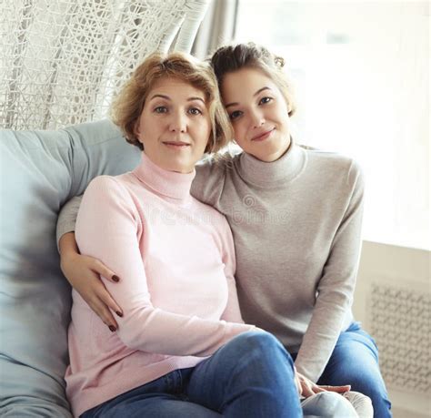 beautiful senior mom and her adult daughter are hugging looking at camera and smiling stock