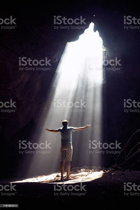 Back View Of A Carefree Man Looking At Sunbeam Entering The Cave Stock