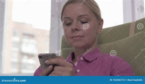 Pretty Blonde Girl Sitting On Armchair And Texting A Message On Her Smartphone Stock Footage