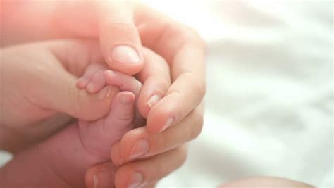 The Hands Of A Mother Gently Touch Her Baby Feet While