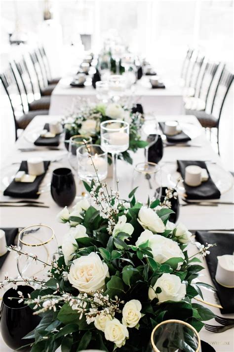 The Table Is Set With Black And White Plates Silverware And Flower