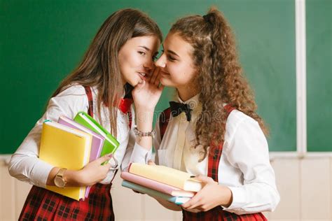 Two Brunette Schoolgirls In School Red Uniforms Stand In A Classroom