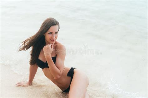 Tanned Girl In Black Swimsuit Posing On Sandy Beach Near Ocean