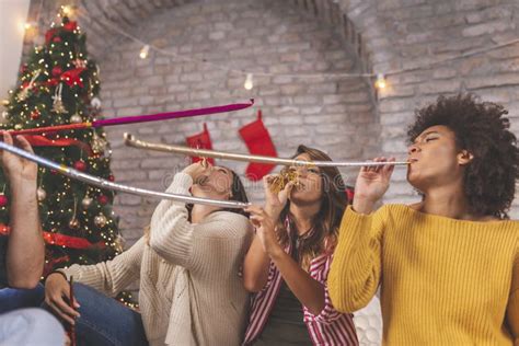 Friends Celebrating New Year At Home Blowing Party Whistles Stock