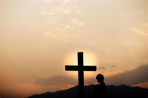 Silhouette Of A Man Prayer In Front Of Cross On Mountain At Sunset