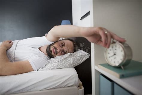 Man Waking Up In His Bedroom And Stopping Alarm Clock Stock Image