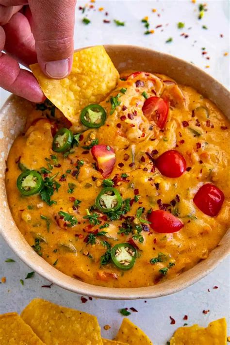 A Hand Dipping A Tortilla Chip Into A Bowl Filled With Salsa And Cheese