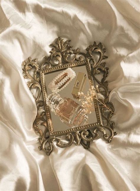 An Ornate Gold Framed Mirror On A White Satin Bed Sheet With Beads And