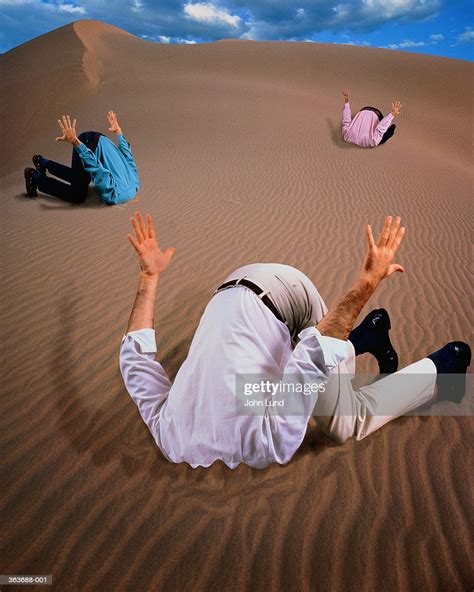 Three Men With Heads Buried In Sand Dune Stock Photo