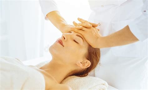 beautiful woman enjoying facial massage with closed eyes in sunny spa center relaxing treatment