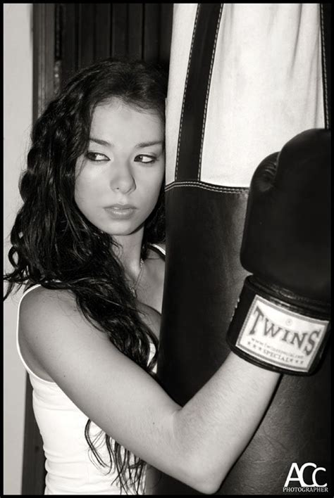 A Woman In White Shirt And Black Boxing Gloves Holding A Punching Bag