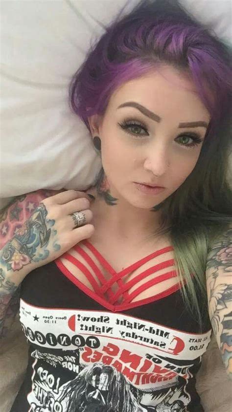 a woman with purple hair and tattoos on her chest laying in bed next to pillows