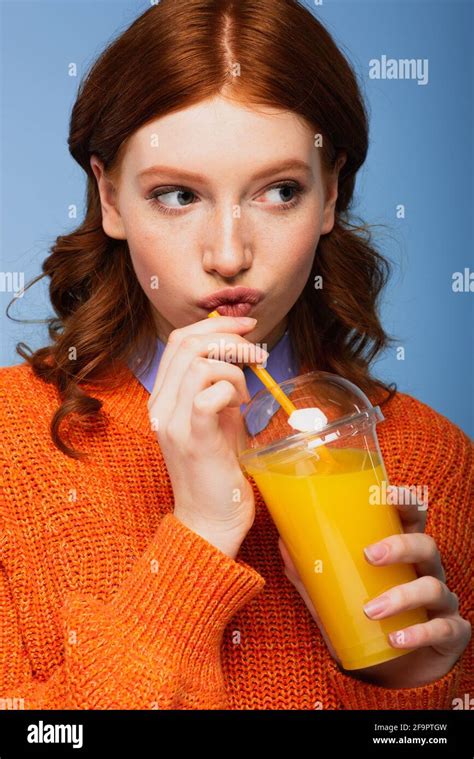 Redhead Woman In Sweater Pouting Lips And Holding Fresh Orange Juice In