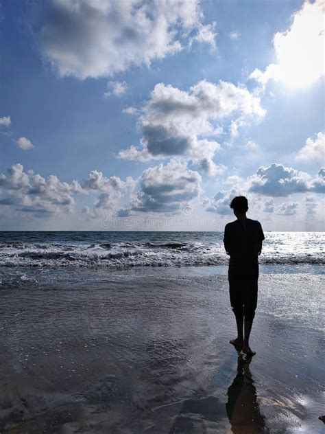 A Person Standing On The Beach Looking At The Ocean Under A Cloudy Sky