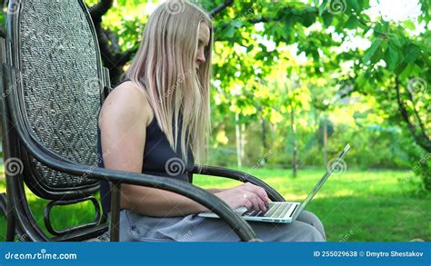 Beautiful Blonde Girl Typing On A Laptop While Sitting In A Rocking Chair Outdoors Stock Footage