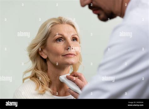 Blonde Woman Looking At Blurred Doctor Examining Her Throat With