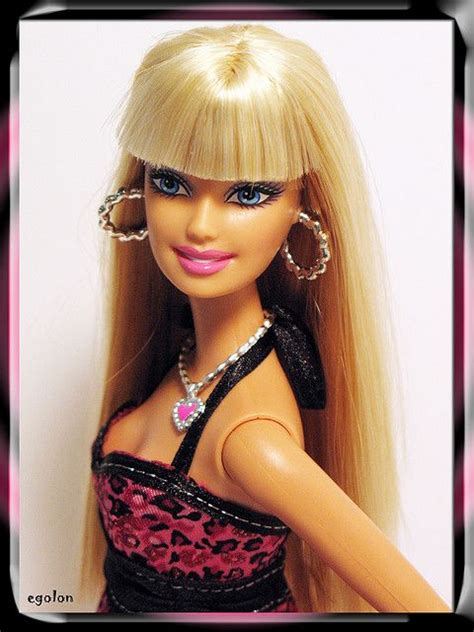 A Barbie Doll With Long Blonde Hair And Blue Eyes Wearing A Black Top Pink Skirt And Earrings