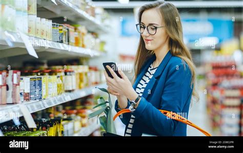 At The Supermarket Beautiful Young Woman Uses Smartphone While
