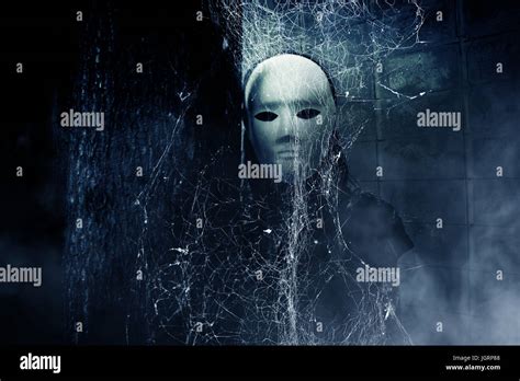 Mysterious woman in black wearing white mask hidden behind spider web