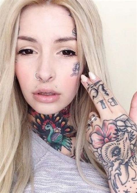A Woman With Tattoos And Piercings On Her Face Is Holding Up Her Hand To The Camera