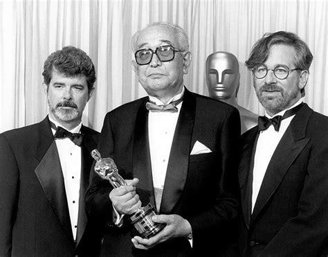 Three Men In Tuxedos Pose With An Award For Best Performance By An Actor