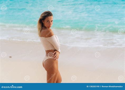 Beautiful Tanned Girl Standing On Beach With White Sand And Blue Ocean