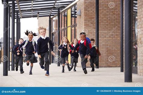 Primary School Kids Wearing School Uniforms And Backpacks Running On