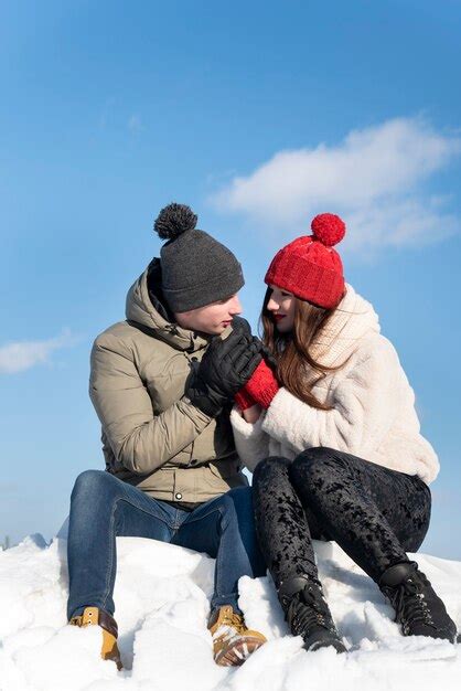 Premium Photo Loving Couple Sits On Snow Against Blue Sky Guy Warms Hands Of His Beloved