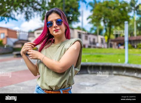 Young Latina Woman In Park With Blue Glasses Arranging Her Fuchsia Hair
