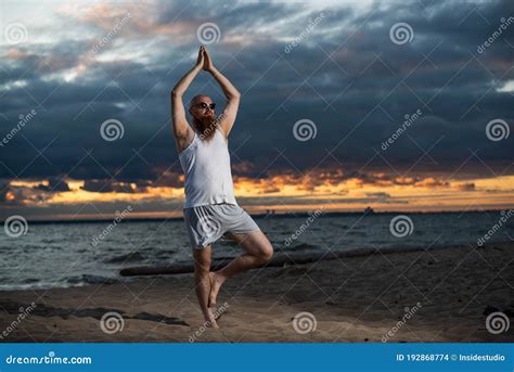 A Bald Man With A Red Beard Practices Yoga On The Beach At Sunset A Funny Dude In A T Shirt And