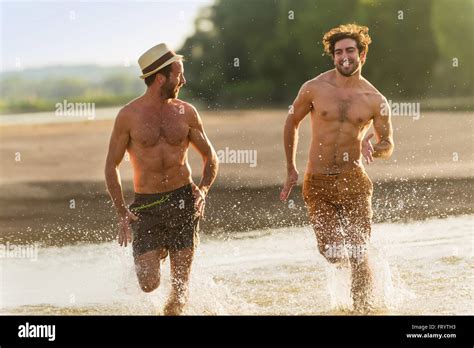 Two Men Friends In Their 30s Are Running In The Water At The Beach
