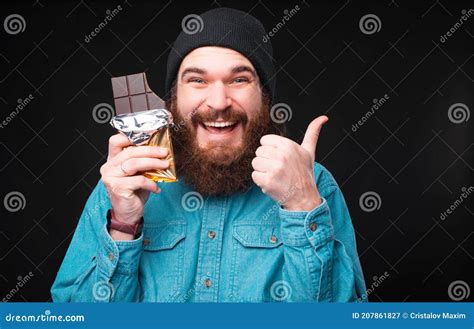 Pouce Barbu Joyeux De Semblant Dhomme Hippie Et Tenant La Barre Du Chocolat Noir Image Stock