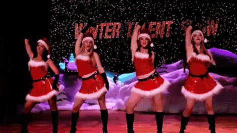 four women dressed in santa claus outfits on stage with their arms up and hands raised