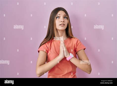 teenager girl standing over pink background begging and praying with hands together with hope