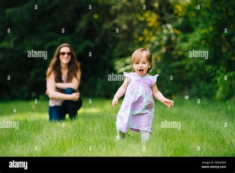 Female Toddler Running Away From Watching Mother In Park Stock Photo
