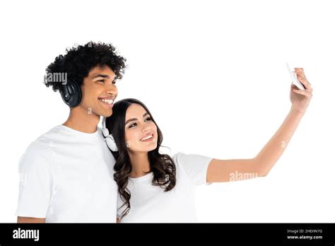 Cheerful Interracial Couple In Headphones Taking Selfie On Mobile Phone Isolated On White Stock