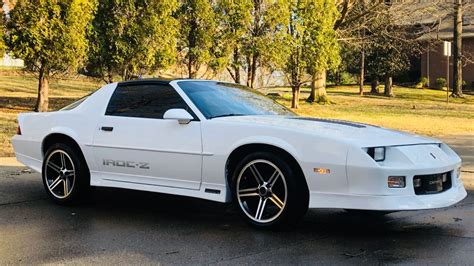 A White Sports Car Parked On The Side Of The Road In Front Of Some Trees