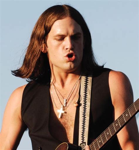 A Man With Long Hair Holding A Guitar And Making A Funny Face At The Camera