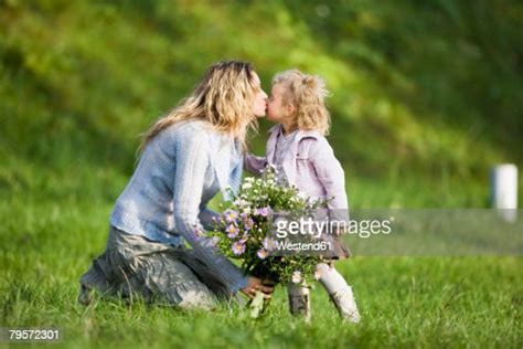 Mother Kissing Daughter Holding Bunch Of Flowers Side View Photo