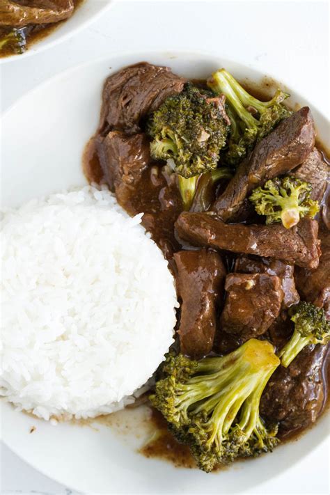 A White Plate Topped With Beef And Broccoli Covered In Sauce Next To Rice