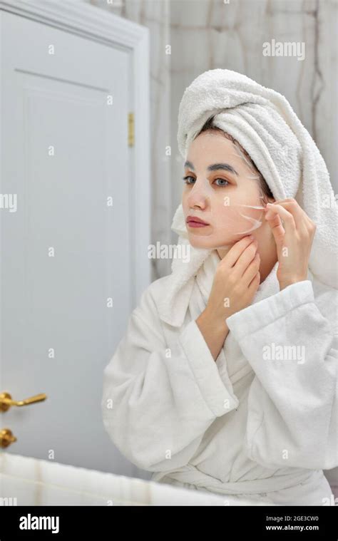 Beautiful Woman In White Bathrobes Applying Sheet Mask On Her Face In