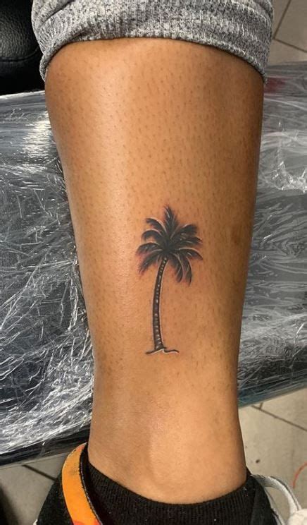 A Small Palm Tree Tattoo On The Side Of A Womans Lower Leg